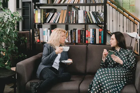 Two people talking warmly on a couch, one holding a cup of coffee