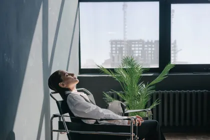 A person relaxed in a chair with eyes closed, resting by a window